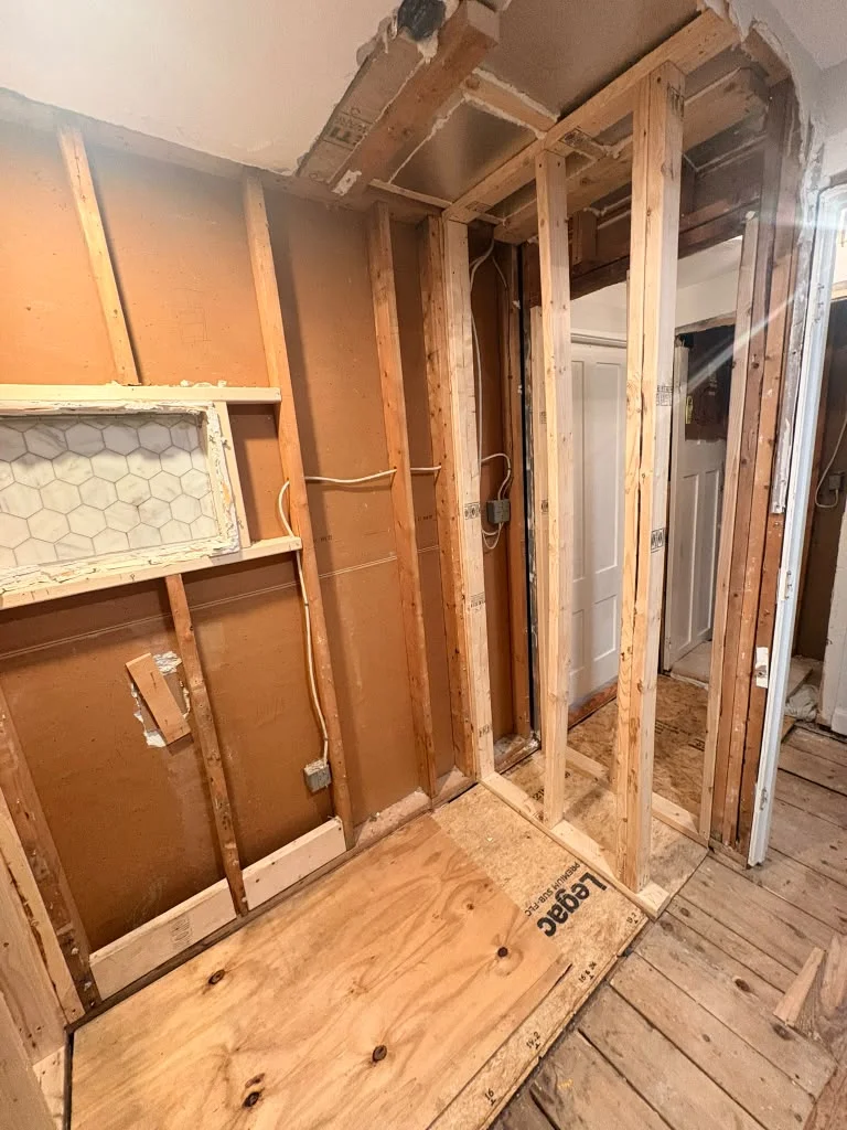 Framed walls with exposed studs, plywood subfloor, and original wood flooring in a renovation. by Boston Strong Plastering in