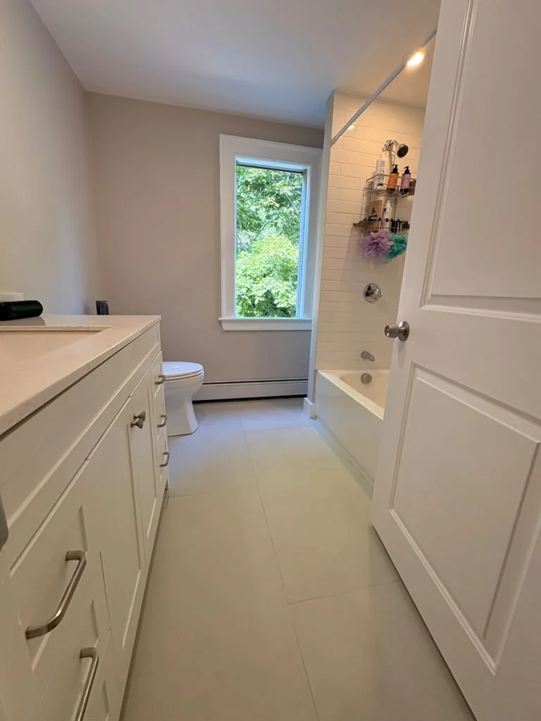 Bathroom with white subway tile shower, light gray floor tiles, and a white vanity. by Boston Strong Plastering in Danvers, M