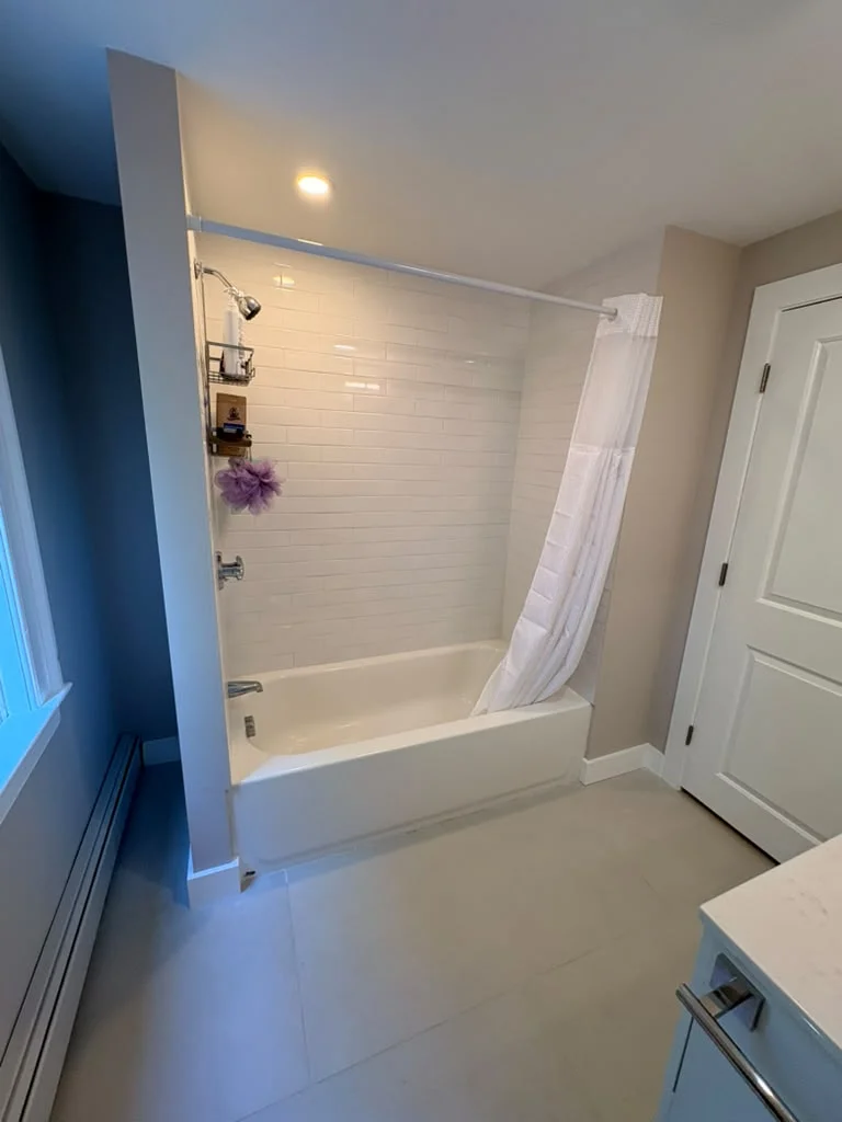 Bathroom with white subway tile shower, light gray floor tiles, and white bathtub. by Boston Strong Plastering in Ipswich, MA