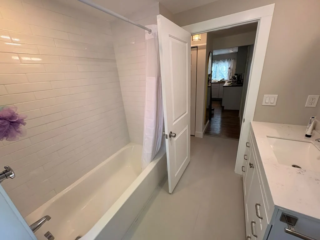 Bathroom with white subway tile shower, white vanity, and light gray floor. by Boston Strong Plastering in Marblehead, MA